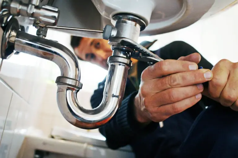 A plumber is using a wrench to tighten the chrome P-trap on a bathroom sink.