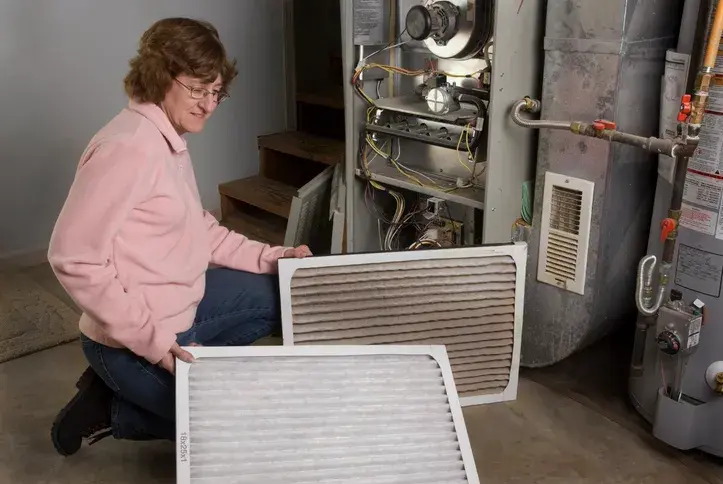 Woman holding a dirty and clean furnace filter next to an open furnace.