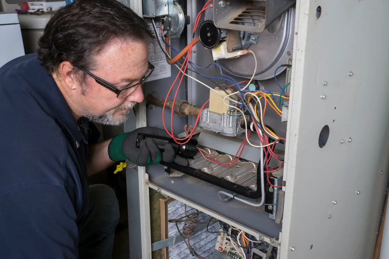 Man in glasses and gloves inspecting the wiring of an open furnace.