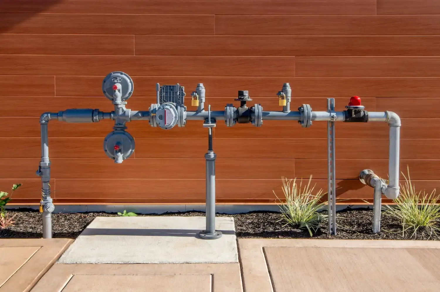 A complex array of gray metal pipes, valves, and a red alarm is installed on a brown wood-paneled wall.