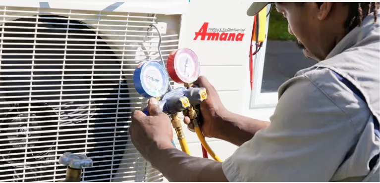 Technician reading refrigerant gauges beside a new Amana system