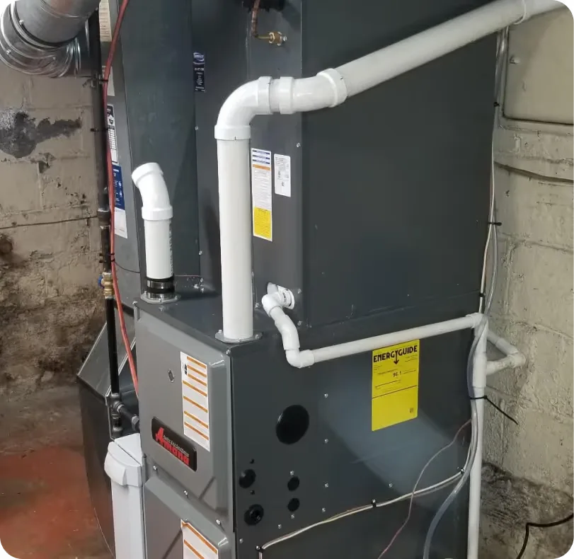 Gray basement furnace connected to white PVC pipes and a metal flue