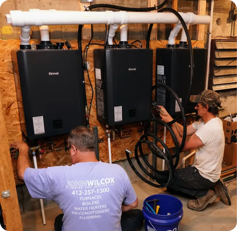 Two technicians installing twin tankless water heaters in a basement